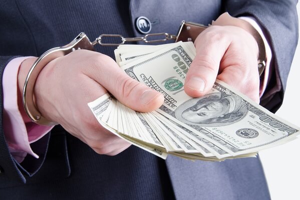 man in handcuffs holding bribery money